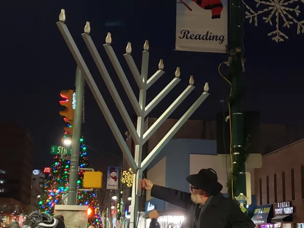 Rabbi Yosef Lipsker, founder and director of Chabad Lubavitch of Berks County, Muhlenberg Township, flips the switch Tuesday on the city's electric menorah on Penn Square. (MICHELLE LYNCH - READING EAGLE)