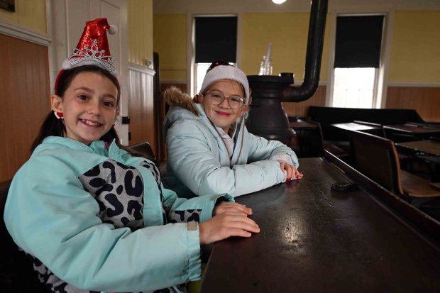 Friendes Victoria Anderson of Shillington and Elyse Pedri of Fleetwood, both 11, sit together in the back of the classroom of the one-room schoolhouse during the Christmas on the Farm at the Pennsylvania German Heritage Center at Kutztown University on Saturday, dec. 6, 2025. They would sit there if they went to school in the early days because it's close to the stove to keep warm. (BILL UHRICH/READING EAGLE)