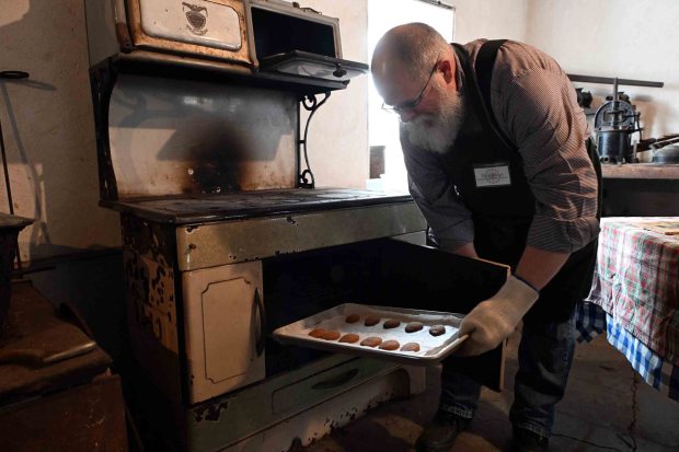 Terry Baker of Carbon County takes some ox-tongue cookies out of the Prizer iron stove in the summer kitchen during the Christmas on the Farm at the Pennsylvania German Heritage Center at Kutztown University on Saturday, dec. 6, 2025.. (BILL UHRICH/READING EAGLE)