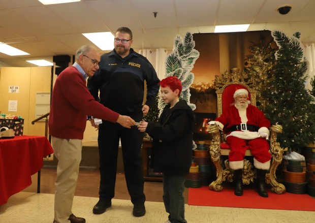 Jim Boscov, CEO of Boscov's Department Store, gives a gift card to Kaden McCoubrey of Schuylkill Valley Elementary, before he goes on a shopping spree with Northern Berks Regional police Sgt. Robert Wood during Crime Alert Berks County's 18th annual Shop with a Cop on Thursday at Boscov's North in Muhlenberg Township. Santa Claus, portrayed by Conrad Vanino, was on hand for the festivities. (Courtesy of Jeffrey Doelp)