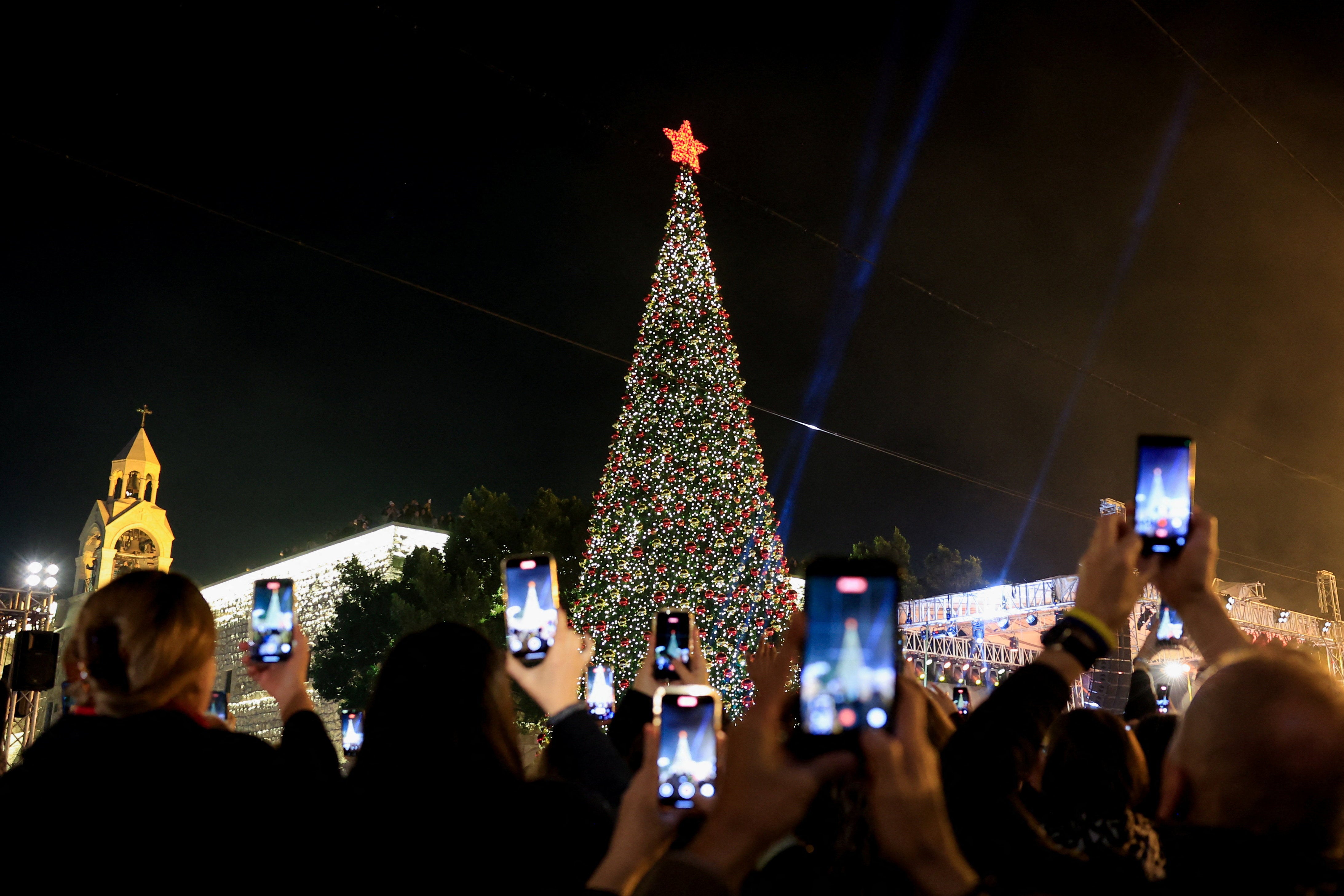 Palestinians use phones to record as a Christmas tree is lit up in Manger Square outside the Church of the Nativity in Bethlehem