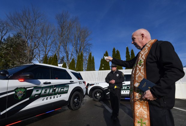 The Rev. Timothy Kennedy annoints the new Jessup police vehicles as acting Sgt. Jason Krawczyk stands by in the Jessup Police Department parking lot in Jessup Wednesday, December 3, 2025. (SEAN MCKEAG / STAFF PHOTOGRAPHER)