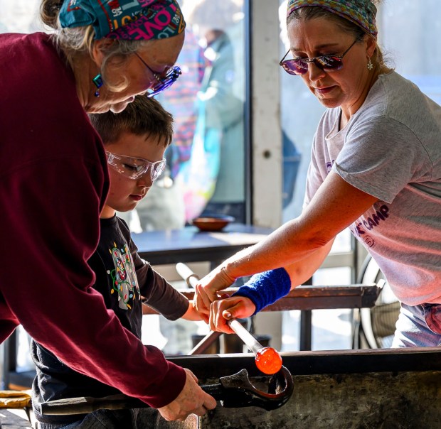Joey Sulovisk, 7, makes a glass ornament from molten glass with the help of Lorraine Wolf and Heidi Wrobel on Saturday, Dec. 20, 2025, during the Hot Glass Experience at Christkindlmarkt in Bethlehem. The German-inspired holiday market, which closes Sunday, Dec. 21, 2025, features artisan vendors, festive treats and family activities. (April Gamiz/The Morning Call)