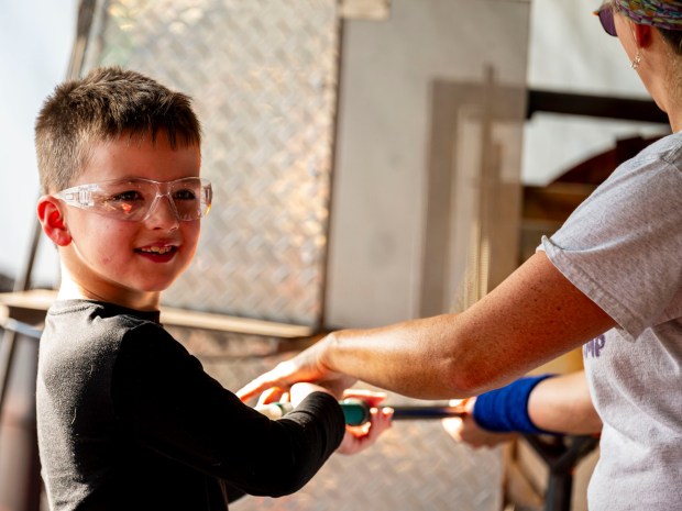 Joey Sulovisk, 7, makes a glass ornament from molten glass with the help of Lorraine Wolf and Heidi Wrobel on Saturday, Dec. 20, 2025, during the Hot Glass Experience at Christkindlmarkt in Bethlehem. The German-inspired holiday market, which closes Sunday, Dec. 21, 2025, features artisan vendors, festive treats and family activities. (April Gamiz/The Morning Call)