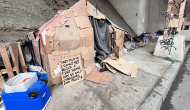 Cardboard shelter under a bridge, with a sign: "They told me I could not build a tiny home out of only cardboard and pallets." Photo taken at homeless Veteran outreach event.