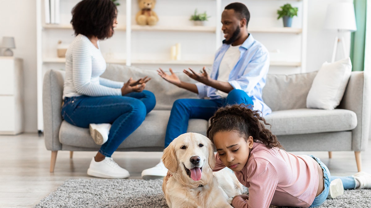 A girl hugging dog while her parents argue
