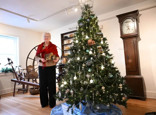 Sharon Donchez, the longtime Trees of Historic Bethlehem co-chair and Historic Bethlehem Museums & Sites' 2025 volunteer of the year, holds an ornament next to the waterworks tree she designed Sunday, Dec. 7, 2025, at the Moravian Museum of Bethlehem in the 1741 Gemeinhaus in Bethlehem. (Amy Shortell/The Morning Call)