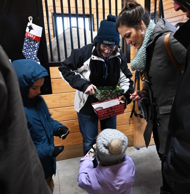 Volunteer MaryAnne Bartone hands out stickers and collectors cards of Bethlehem police horses as people visit during the Holiday with the Horses open house Sunday, Dec. 7, 2025, at the Bethlehem mounted police unit's barn. (Amy Shortell/The Morning Call)