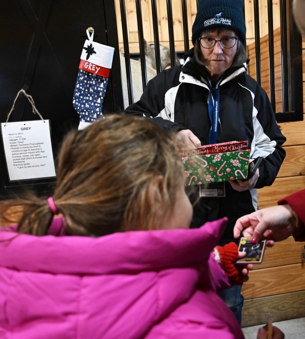 Volunteer MaryAnne Bartone hands out stickers and collectors cards of Bethlehem police horses as people visit during the Holiday with the Horses open house Sunday, Dec. 7, 2025, at the Bethlehem mounted police unit's barn. (Amy Shortell/The Morning Call)