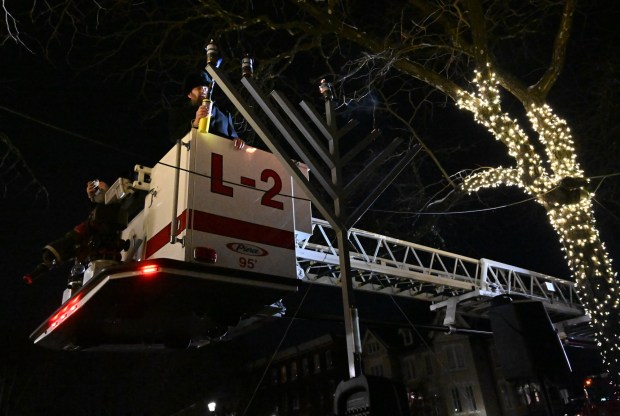Rabbi Yaacov Halperin and Bethlehem firefighters light three candles Monday, Dec. 15, 2025, on a Hanukkah menorah at Payrow Plaza in Bethlehem. Monday was the second night of the eight-day Jewish Festival of Lights. The third candle is the shamash, a ninth candle that is used to light other candles. (Amy Shortell/The Morning Call)