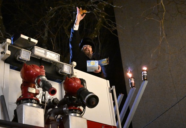 Rabbi Yaacov Halperin throws chocolate gold coins, known as gelt, from the bucket of a fire truck after lighting three candles Monday, Dec. 15, 2025, on a Hanukkah menorah at Payrow Plaza in Bethlehem. Monday was the second night of the eight-day Jewish Festival of Lights.  (Amy Shortell/The Morning Call)