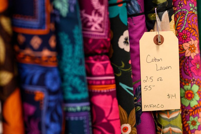 Assorted colorful patterned cotton lawn fabrics hang with a handwritten price tag stating 