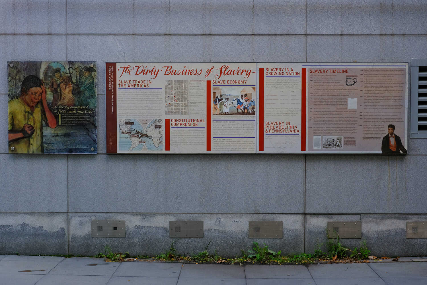 Displays from an exhibit are fixed on a gray wall. One of them reads, “The Dirty Business of Slavery.”