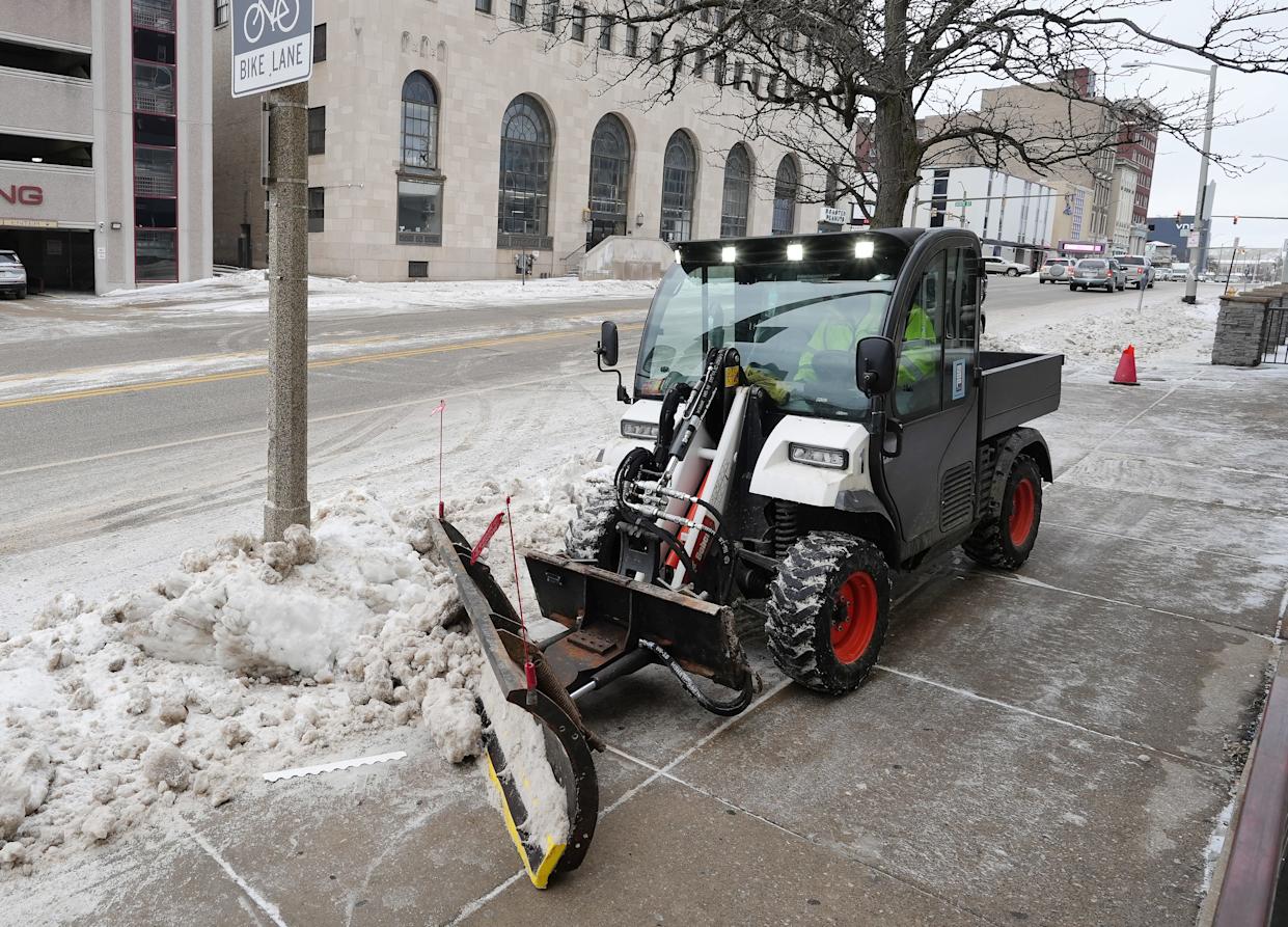 Erie Downtown Partnership Ambassador Derek Smith clears snow near a bus stop, with single-digit temperatures outdoors.