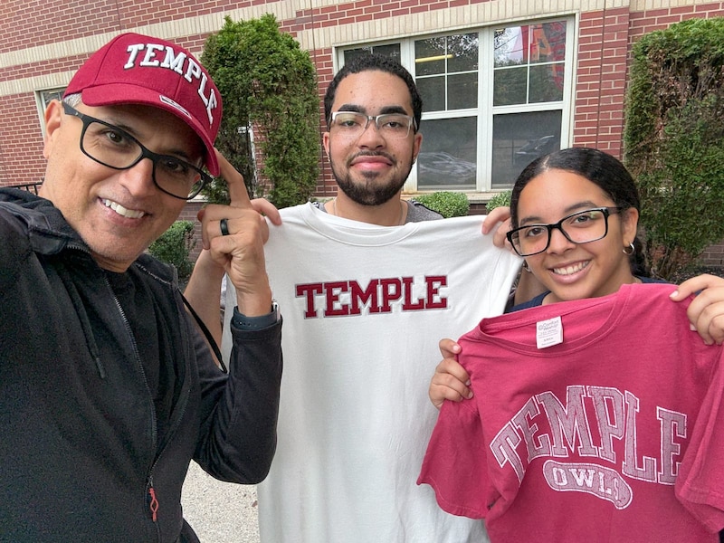 Three people stand next to each other posing for a photograph. Two of the students are holding up t-shirts.