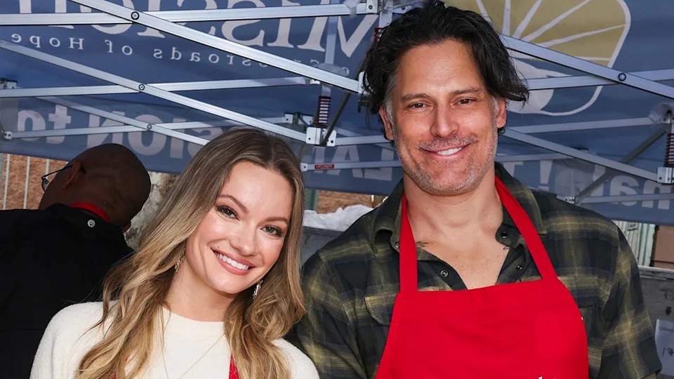 Caitlin O'Connor wearing a white sweater standing next to Joe Manganiello wearing a plaid shirt and a red apron.