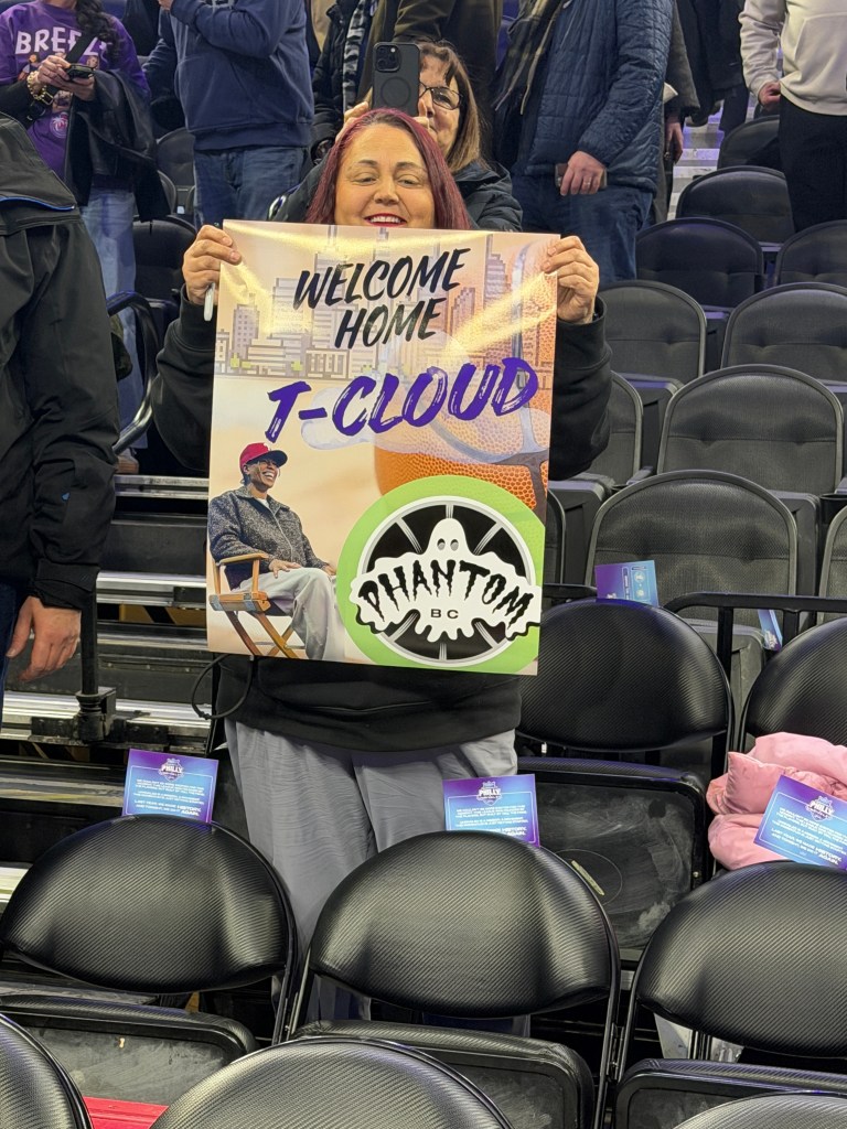 A fan holds a colorful sign for Natasha Cloud. It reads "Welcome home T-Cloud" and has her photo and her team's logo.