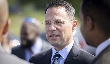 Pennsylvania Governor Josh Shapiro speaks with attendees during an outdoor public event, wearing a dark suit and striped tie.