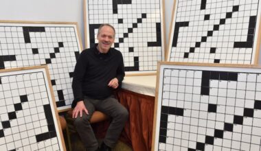 Will Shortz, founder and director of the American Crossword Puzzle Tournament, sits amid large crossword puzzle whiteboards used in the tournament's championship rounds.