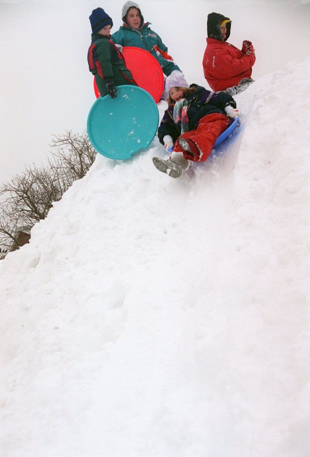 Cara Costelloe, 9, right front, rides her snow saucer down a huge pile of snow left by snowplows in the Rodale Press parking lot on North Sixth St. in Emmaus after the blizzard of 1996, Jan. 9, 1996. (Betty E. Cauler/The Morning Call)