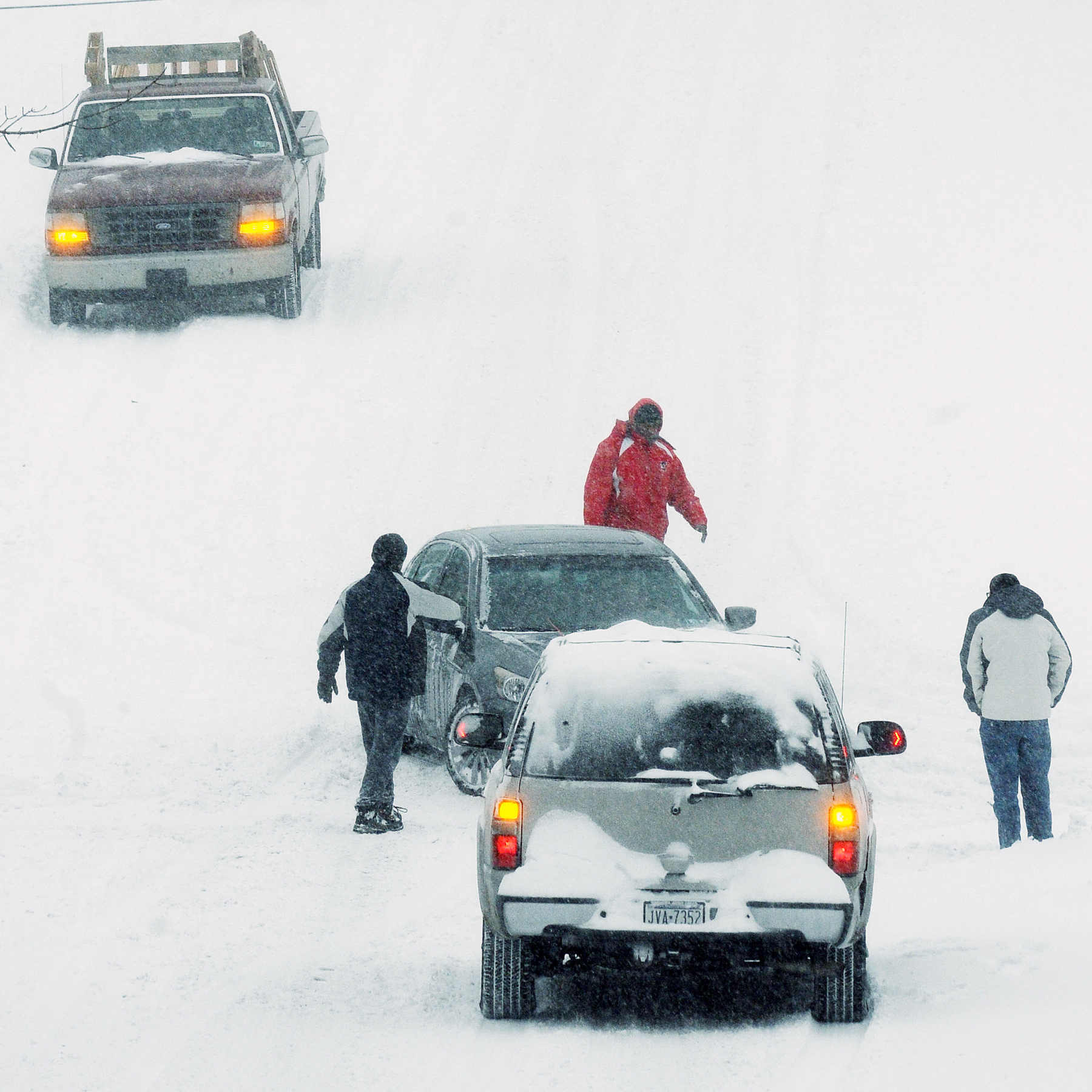 Three pedestrians work to help a stuck car on a...