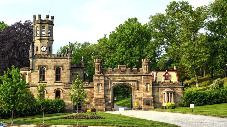 Gatehouse of Allegheny Cemetery, a majestic brown stone building with towers surrounded by green trees under a cloudy sky