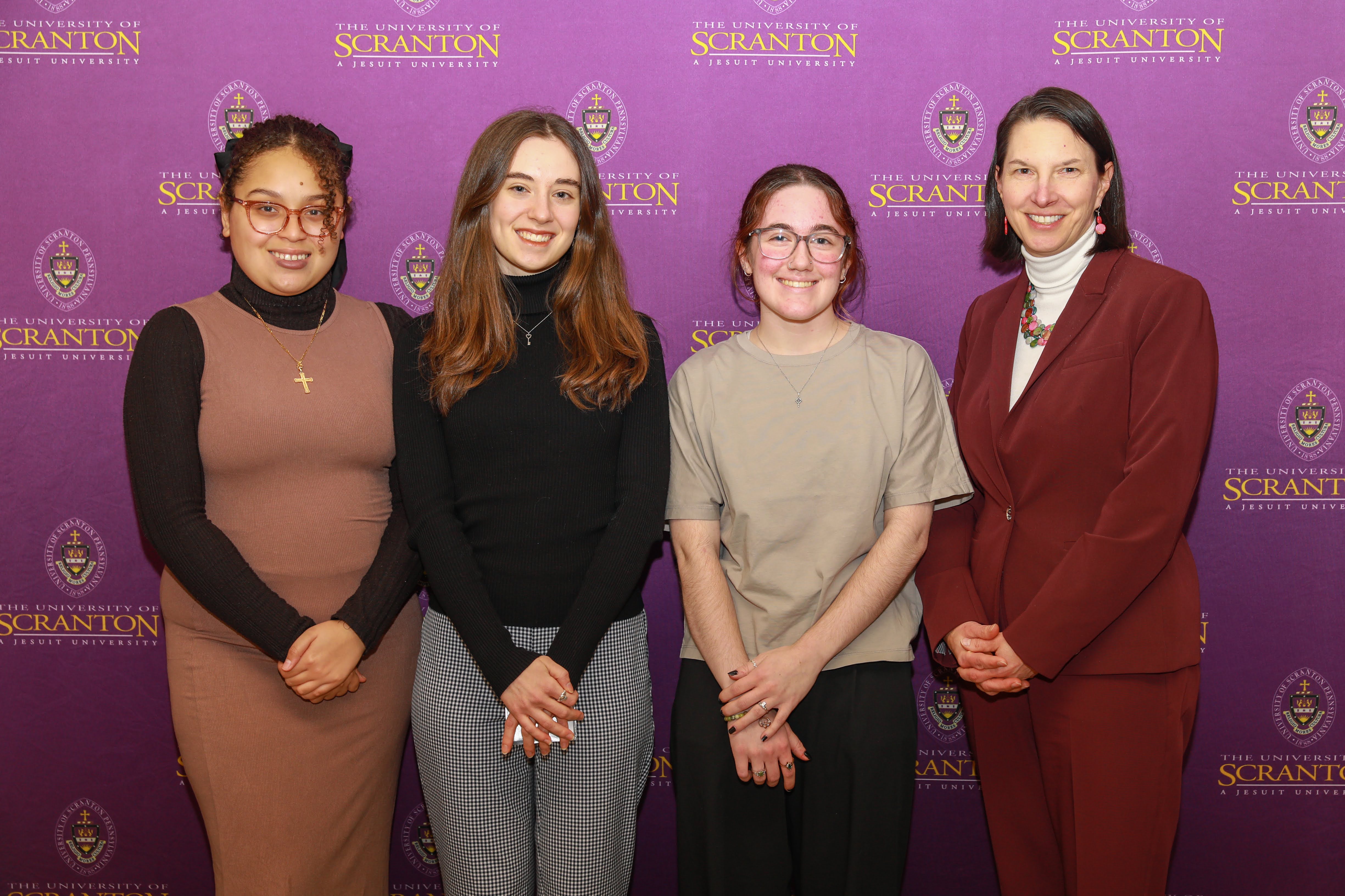 Group of four individuals standing in front of a purple backdrop featuring the University of Scranton logo.