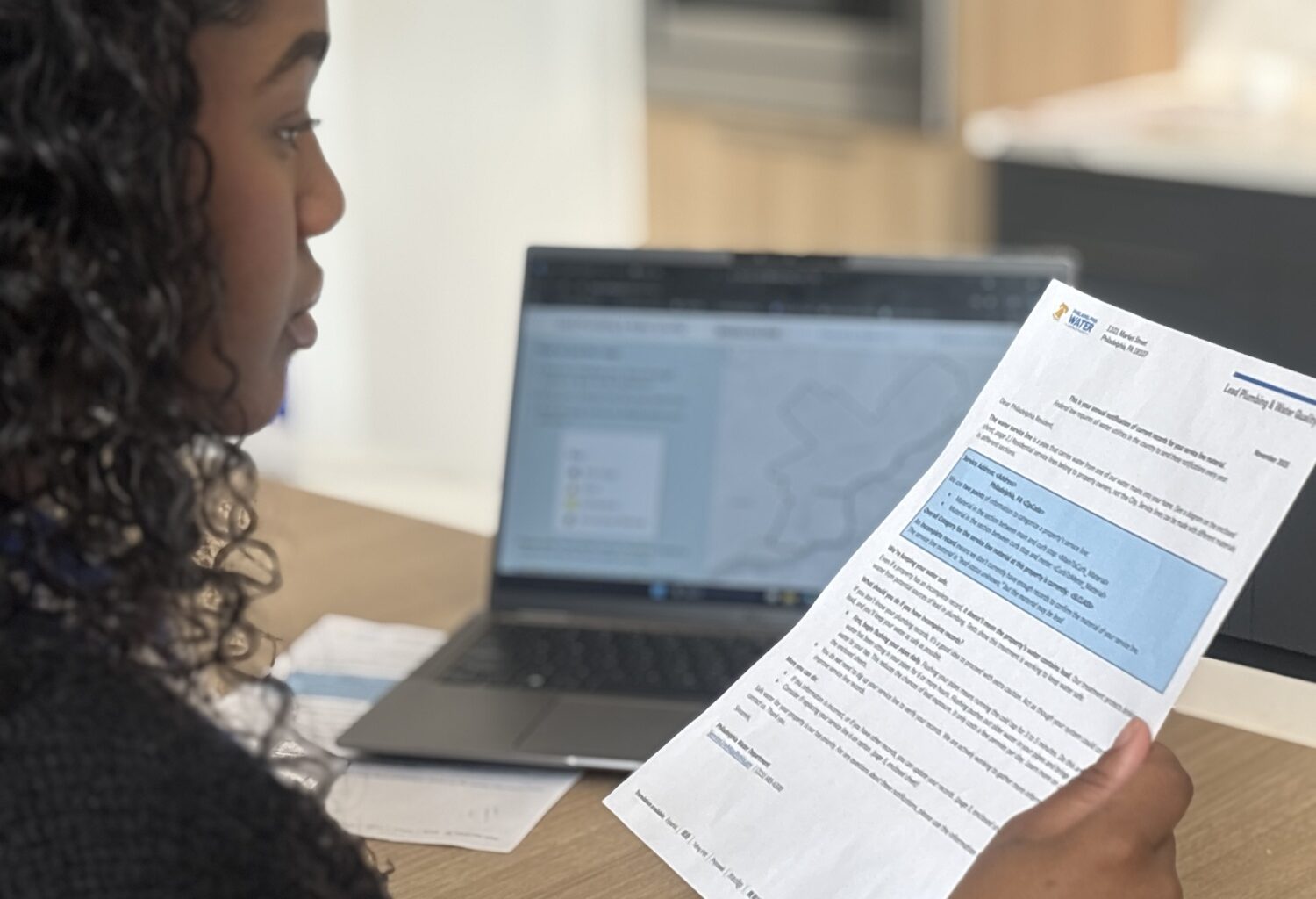 A young woman reads a letter with a laptop computer in the background