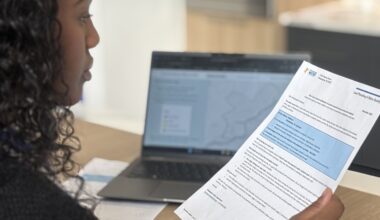 A young woman reads a letter with a laptop computer in the background