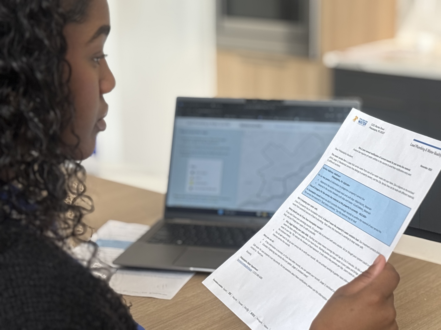 A young woman reads a letter with a laptop computer in the background