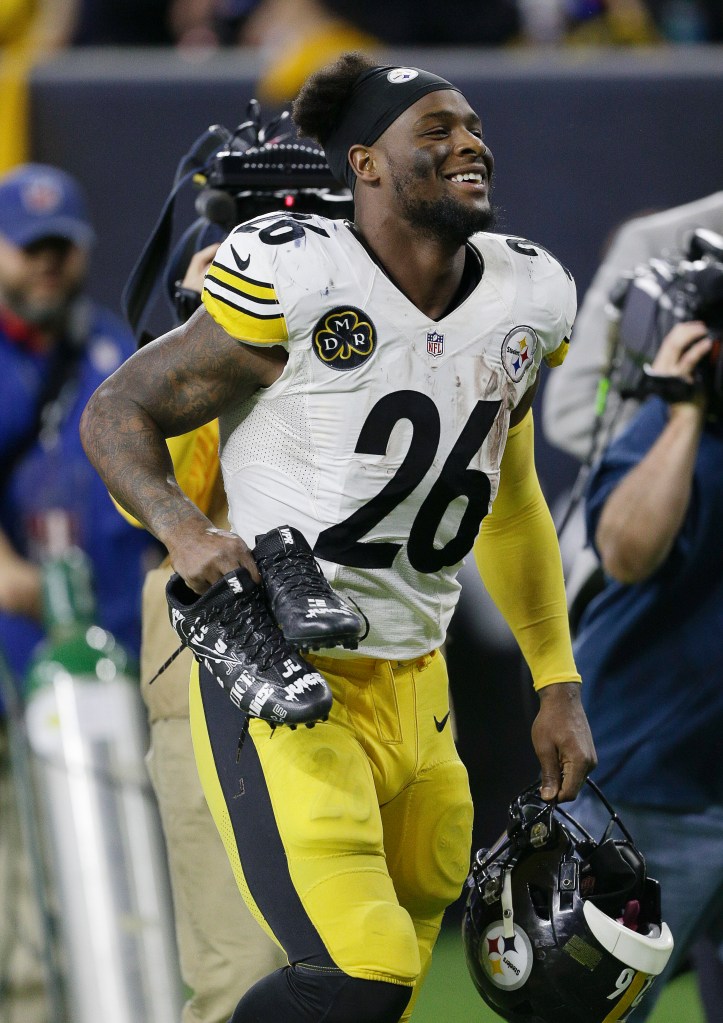 Pittsburgh Steelers player Le'Veon Bell smiling while holding his football helmet and cleats.