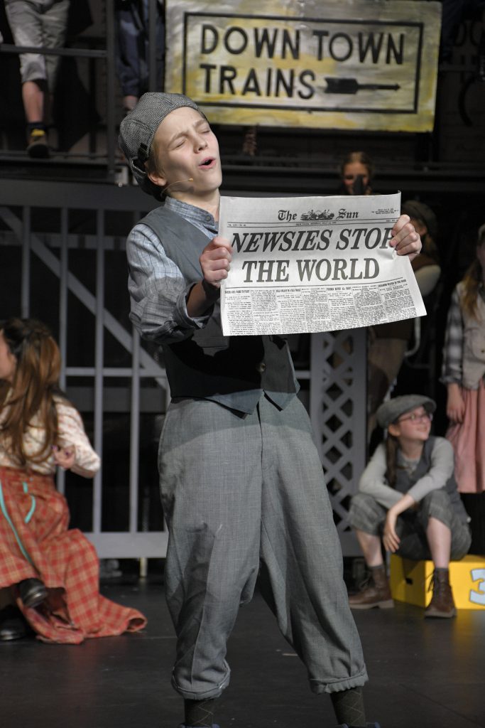 student singing on stage holding newspaper
