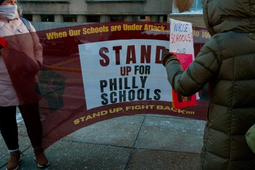 People holding up a large banner at the rally in front of the School District building