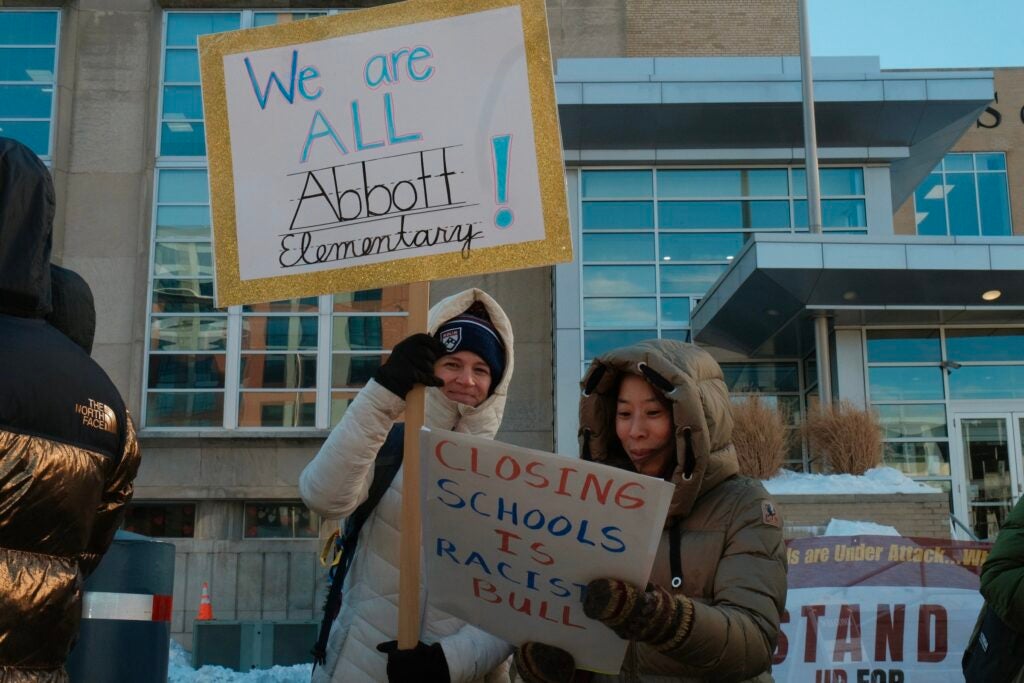 Two people holding up signs at a rally in front of the Philadelphia School District
