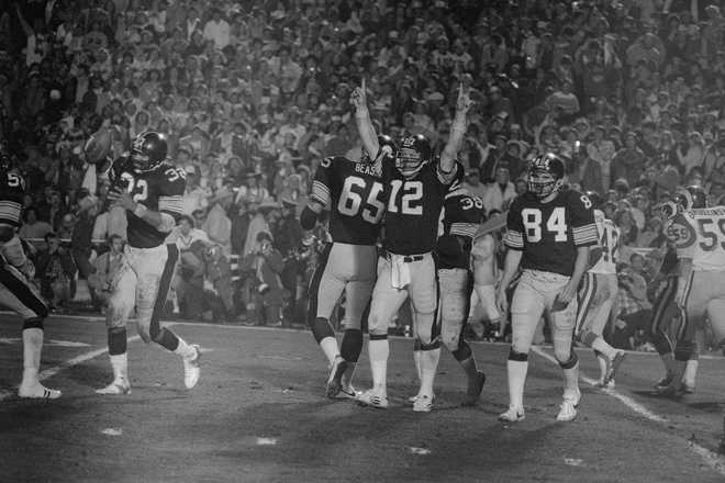 Steelers quarterback Terry Bradshaw, who was named MVP of Super Bowl XIV, holds his hands up in victory as Franco Harris, who scored his second touchdown, carries the ball off the field.