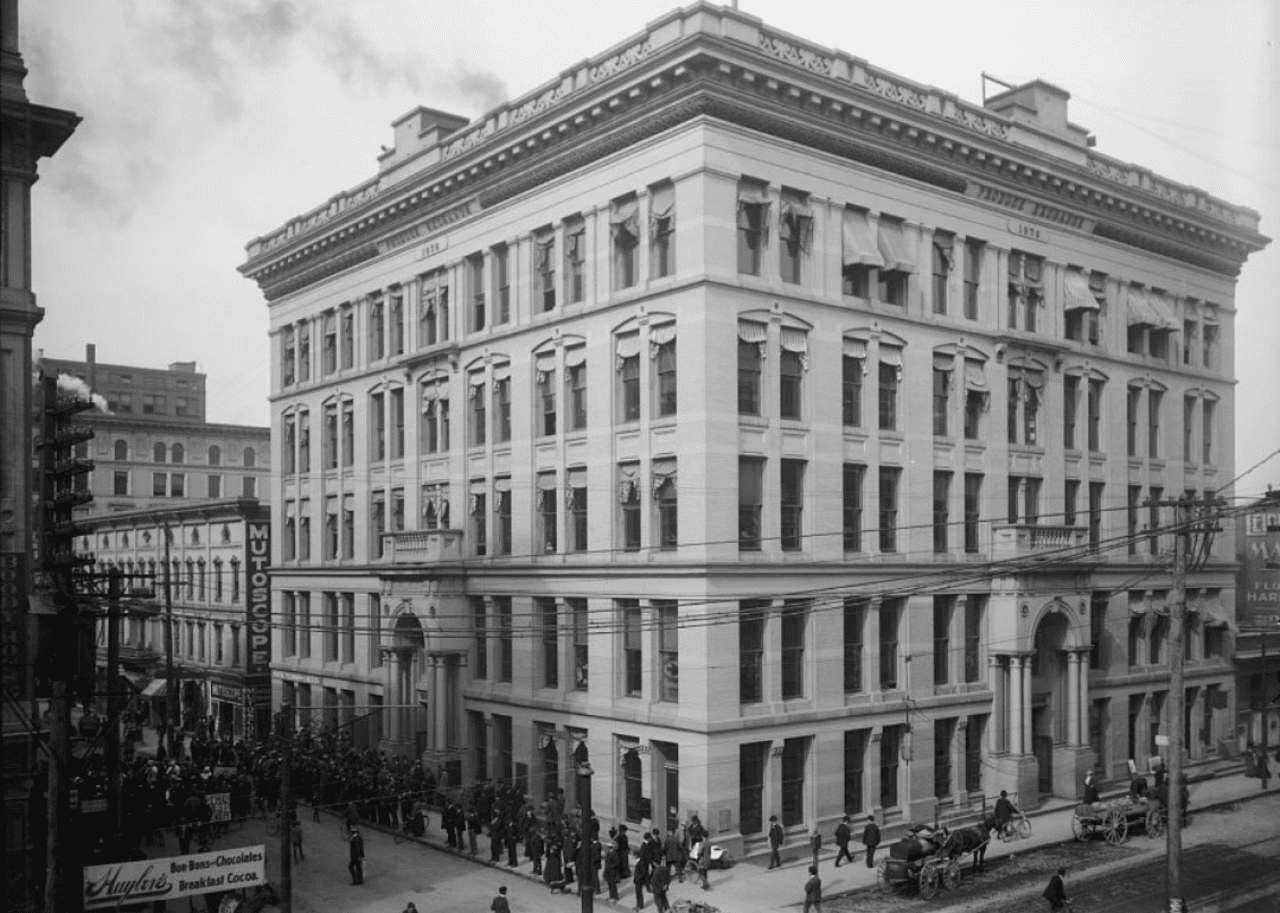 Six story stone building in downtown with people on sidewalk
