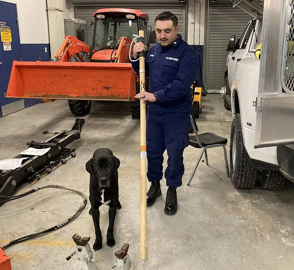 Coast Guard Petty Officer 2nd Class Gage Downer demonstrates how to use an ice staff, a wooden stick with a metal tip, to find unsafe areas of ice during a rescue attempt. He is joined by Zeus, the security dog at the Coast Guard Station Erie at Presque Isle State Park.