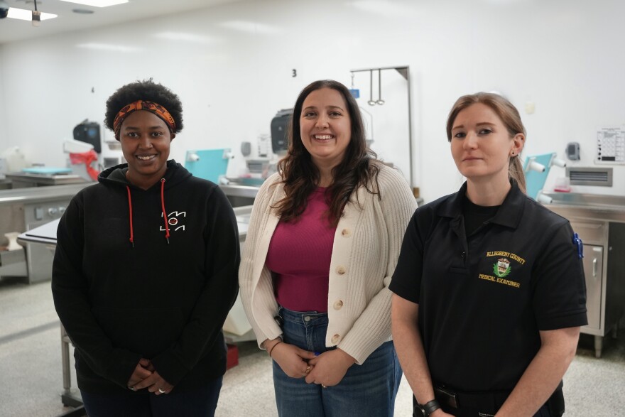 Three women stand in an autopsy lab at the Allegheny County Medical Examiner's Office. 