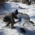 A woman bends down at a small creek in the snow.