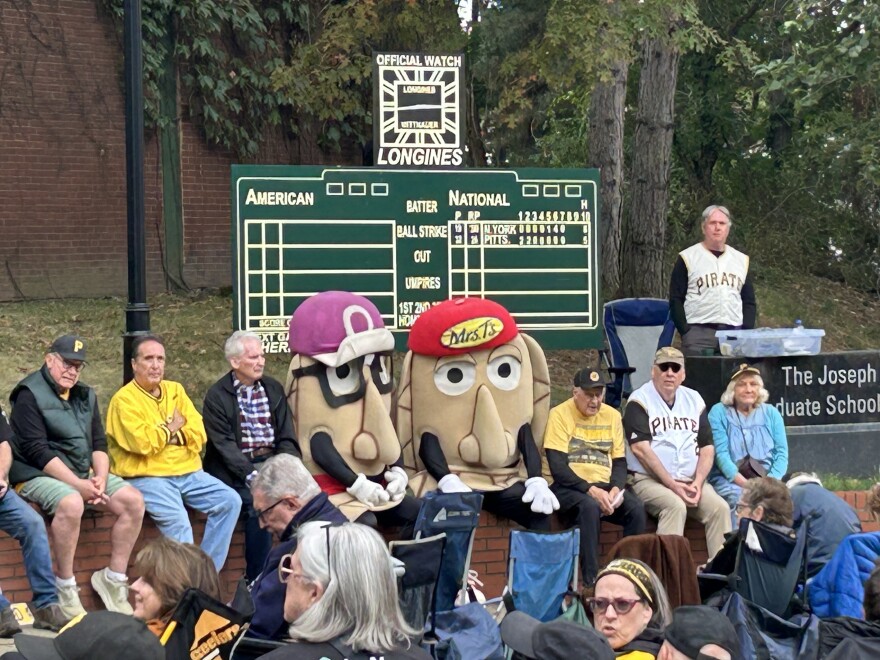 A group of people sits on bleachers outside the former Forbes Field outfield wall.