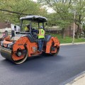 An orange paving machine rolls along black pavement on a street.