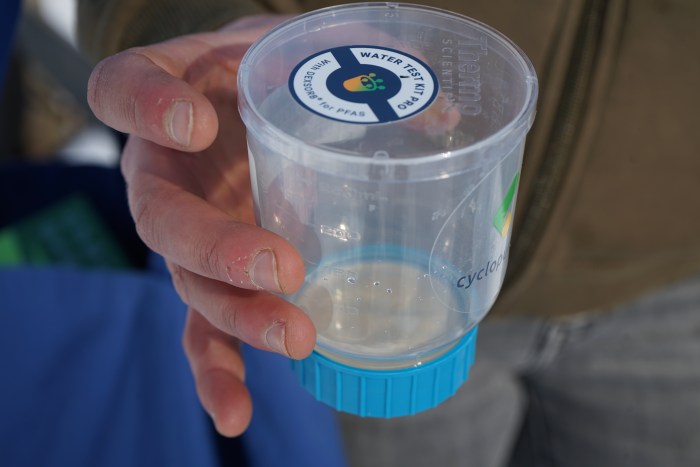 A hand holds a clear plastic cup with a blue cap at the bottom.