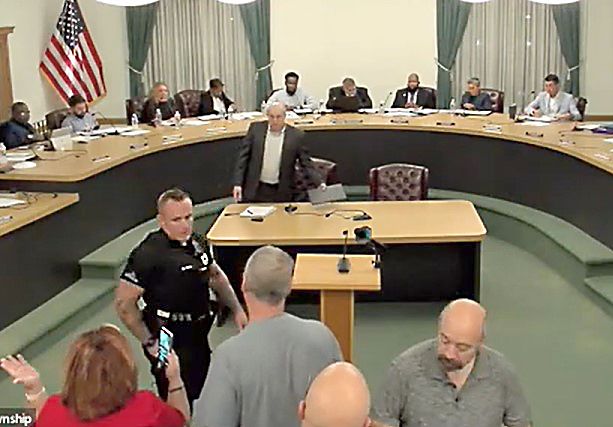 An Upper Darby police officer ushers residents who didn't get a chance to speak back to their seats. (YOUTUBE SCREEN CAPTURE)