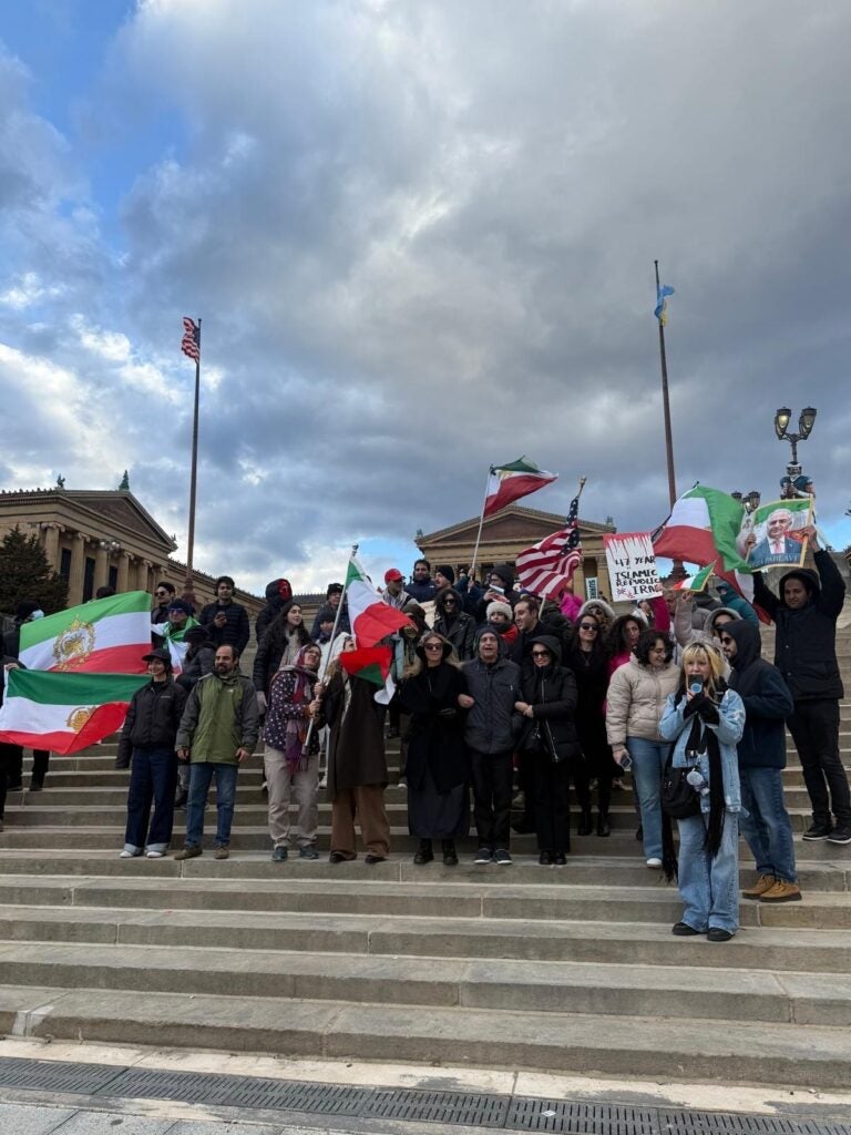 Iranian Americans stand on steps outside in Philadelphia holding Iranian flags