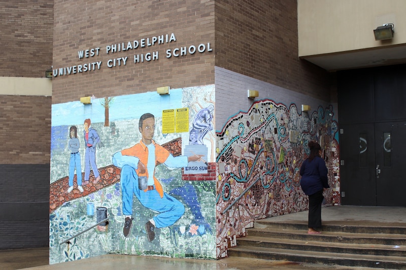 A photograph of the front of a school brick building with a person walking up the sidewalk.
