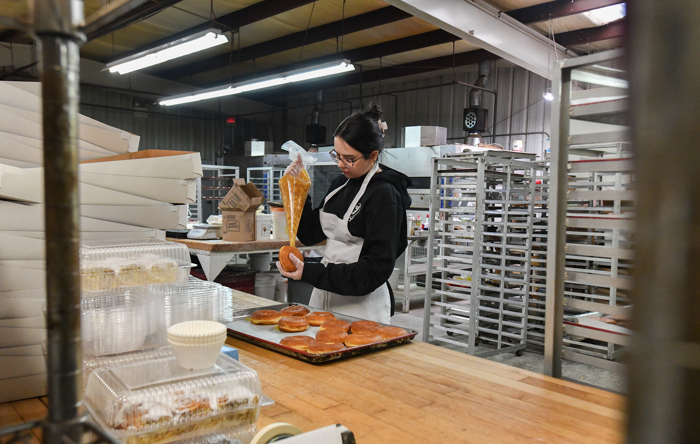 Manager Candace Fox fills pÄczki doughnuts with apple filling Monday,...