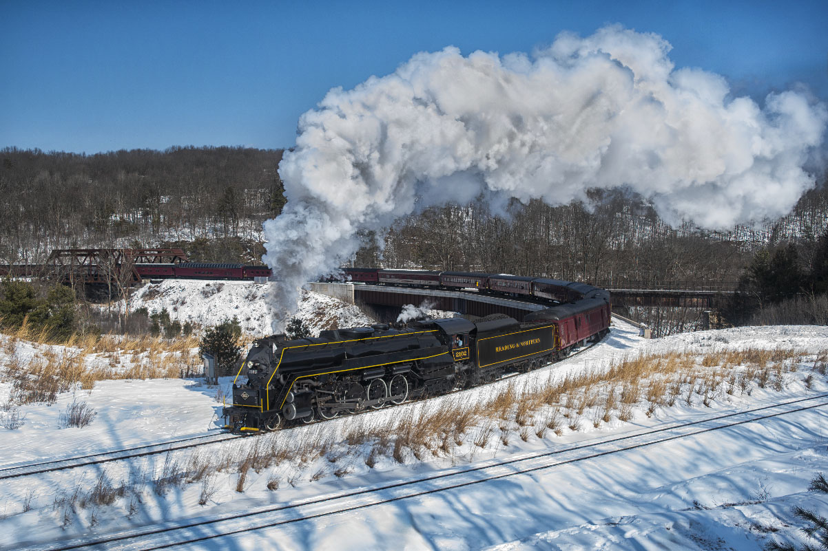 Black steam locomotive on a curve in a snowy landscape. Reading & Northern No. 2102 winter rambles.