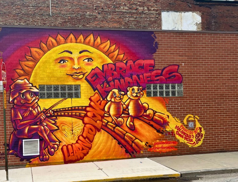 A mural shows a frog, dog and cat all getting along with the phrase "embrace kindness" written above.