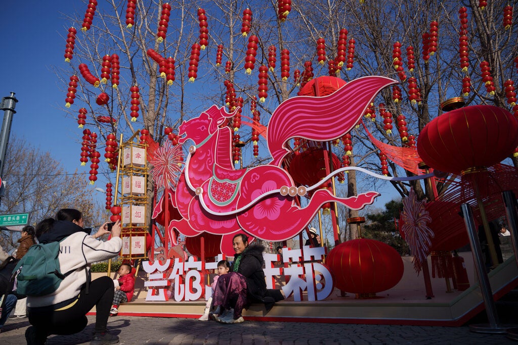 Visitors pose for photos beside a decorative pink horse installation surrounded by red lanterns during the second day of Lunar New Year celebrations at a temple fair in Beijing