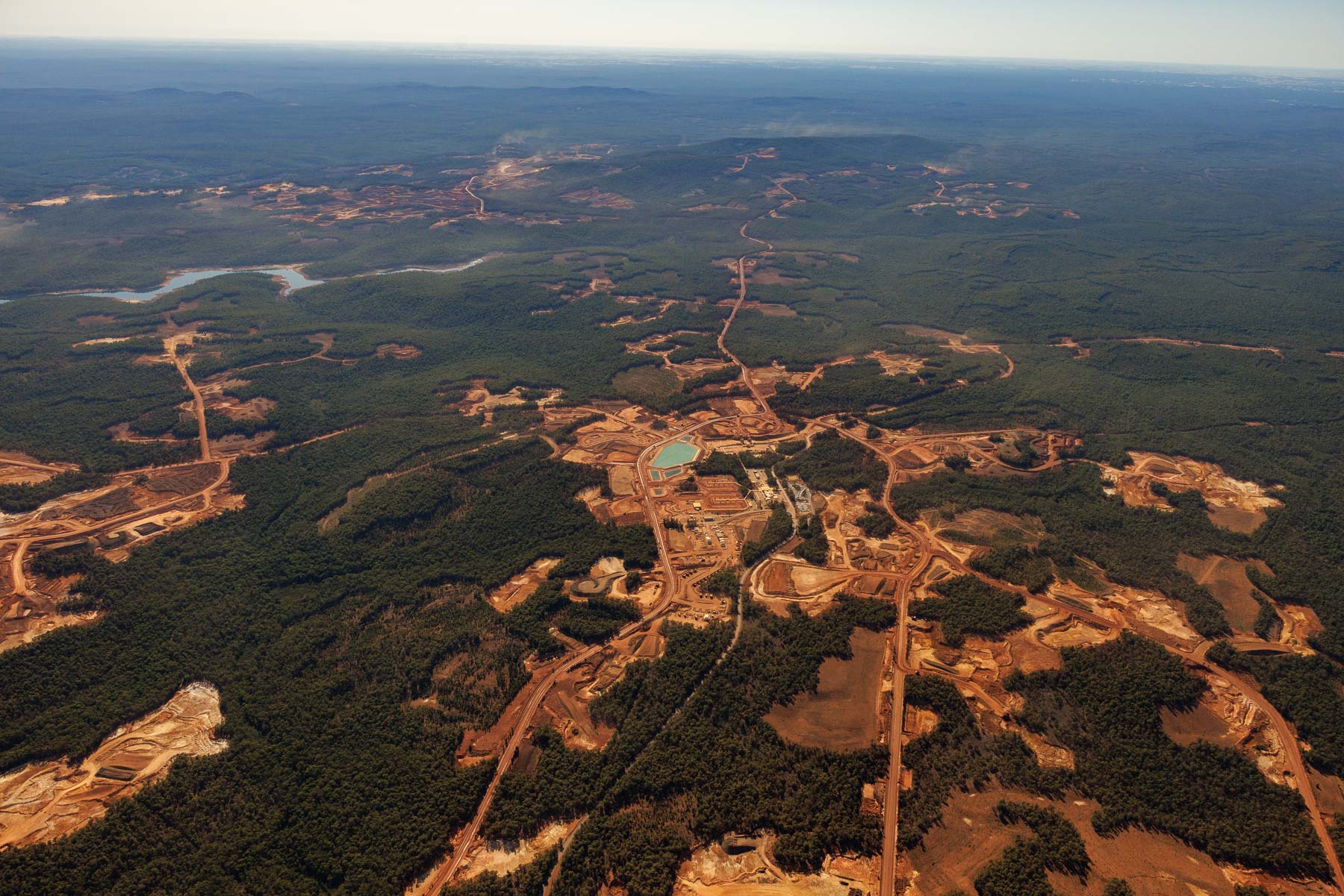Aerial view of a large mining operation with cleared land, roads, facilities, and surrounding forested areas.